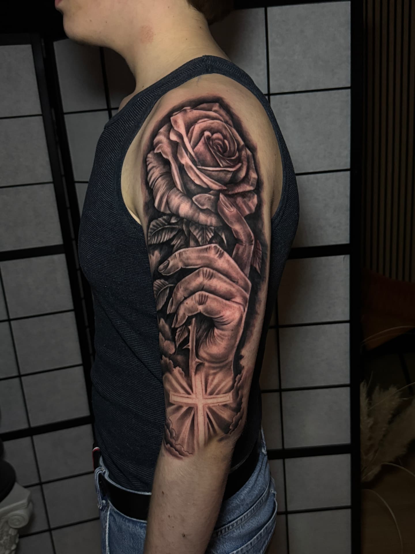 Realistisches Schwarz-Grau-Arm-Tattoo mit Rose, Hand und leuchtendem Kreuz bei Omilian Tattoo bei Kiel