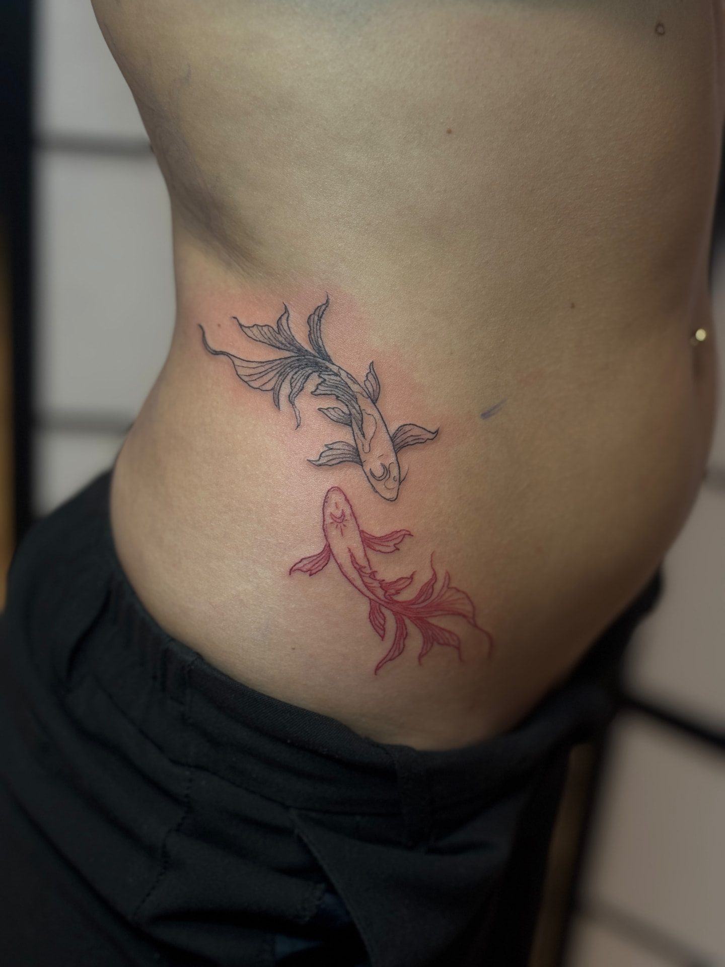 Fine-Line-Tattoo mit zwei Koi-Fischen in Schwarz und Rot von Omilian Tattoo bei Kiel
