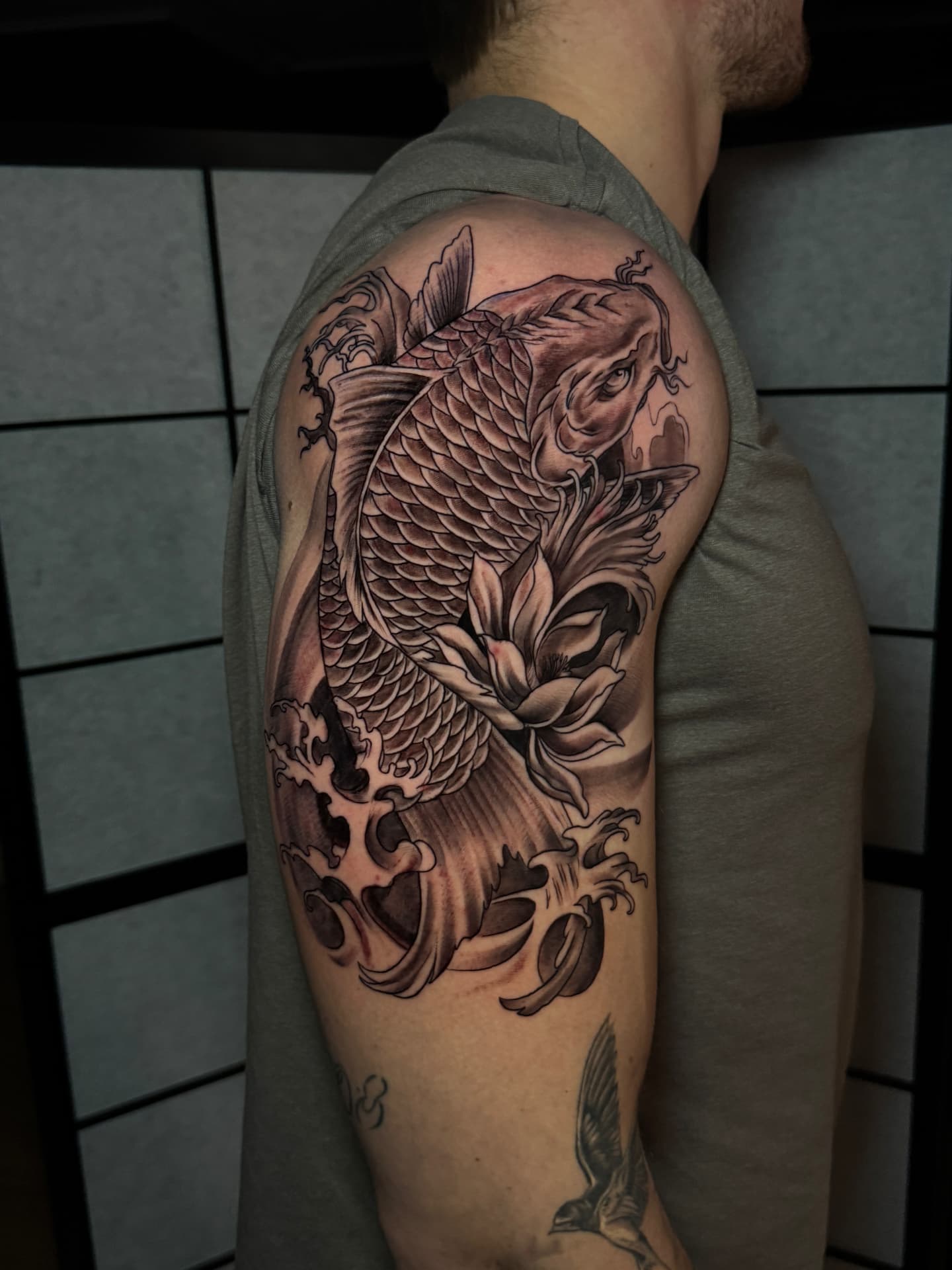 Realistisches Koi-Karpfen-Tattoo mit Lotusblüte und Wellen auf der Schulter bei Omilian Tattoo in Laboe bei Kiel